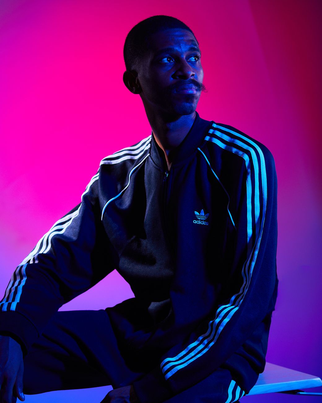 a man in adidas tracksuit sitting on a chair